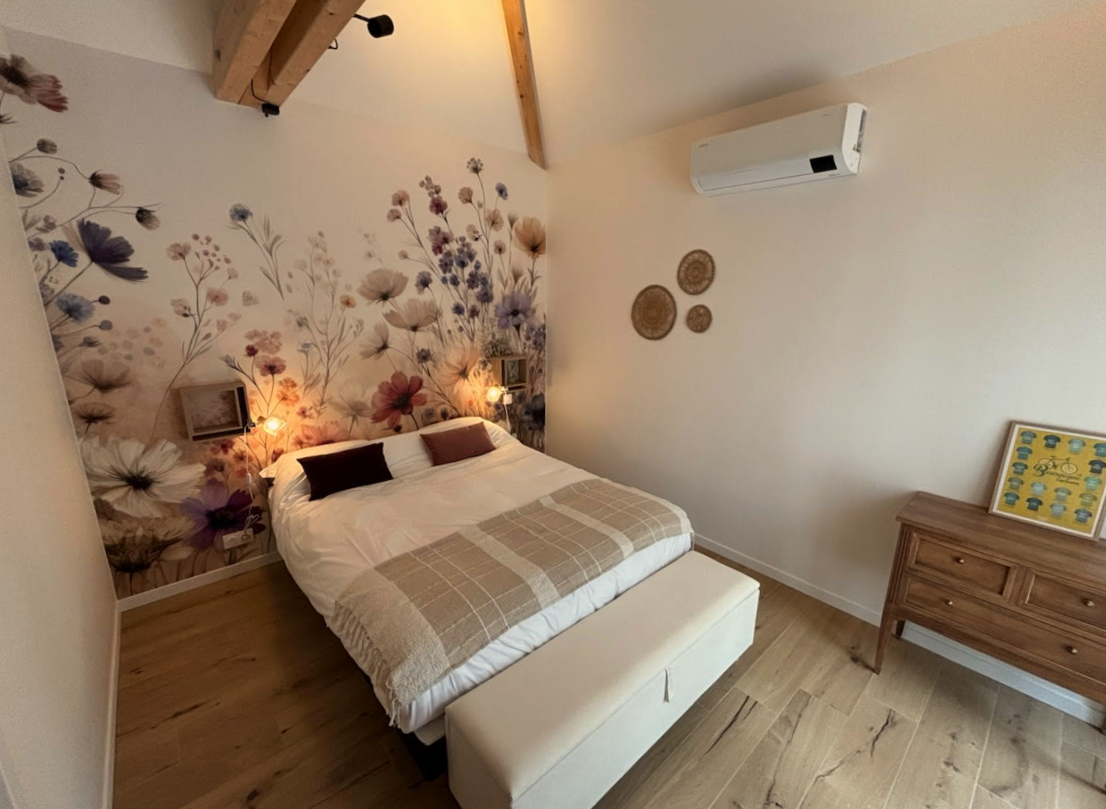 Photo d'une chambre à coucher cosy avec papier peint floral au mur, charpente apparente et climatisation.